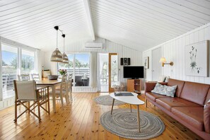 A spacious living area with a wooden floor, a brown leather sofa, a white table, and a dining set. - Idyllic holiday home charm in Nr. Lyngby (Løkken)
