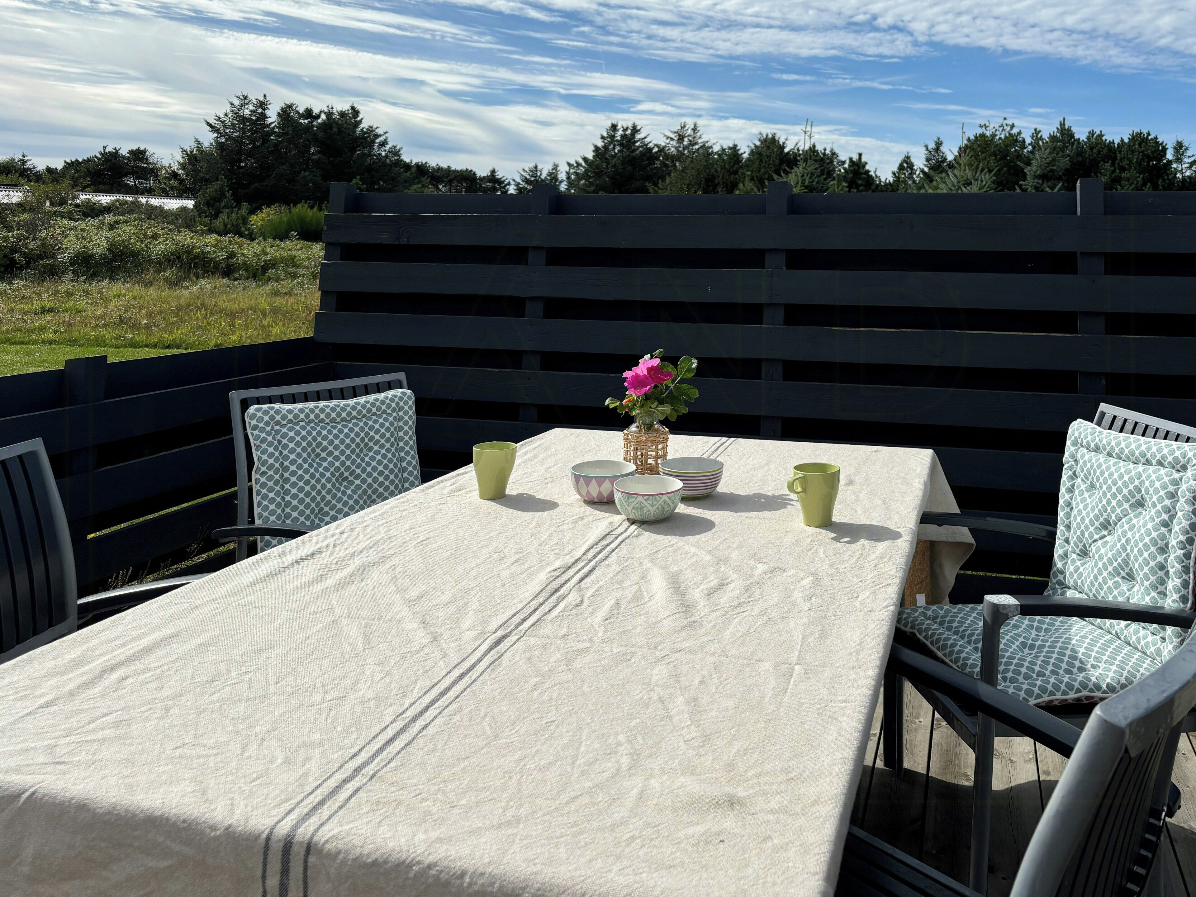 Une table dressée à l’extérieur, avec des chaises, une nappe et un vase rempli de fleurs.