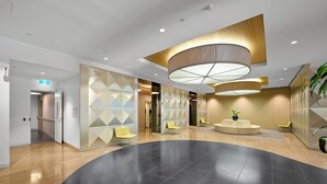 A modern lobby with a curved black floor, geometric wall panels, and a central seating area with a plant. - Exclusive Stays - Southbank Grand (Southbank)