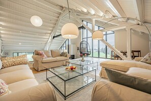 Ein geräumiges Loft mit hohen Decken, großen Fenstern, einem Hängekorbsessel und einem Glastisch.