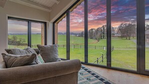 A room with a large window, a sofa, and a view of a green field. - Panoramic view in design apartment the Schlei (Thumby)