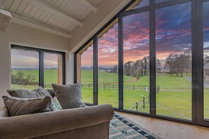 Ein Zimmer mit großem Fenster, einer Couch und Blick auf ein grünes Feld.