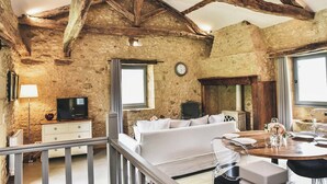 A rustic room with exposed beams, stone walls, a sofa, a dining table set, and a television. - Charming mas with medieval church views (Sainte Croix)