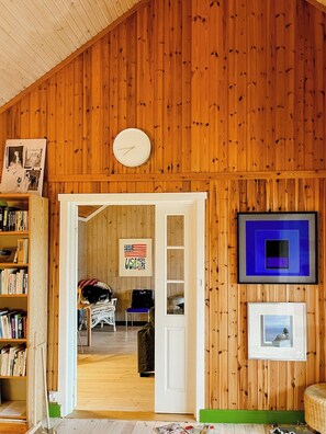 Une pièce aux murs en bois, avec une horloge, un drapeau américain encadré, une œuvre d’art encadrée dans un cadre bleu, et une porte donnant sur une autre pièce.