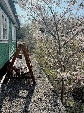 Un ensemble de jeux d’extérieur en bois avec un coussin blanc, un bâtiment vert et des arbres en fleurs de cerisier.