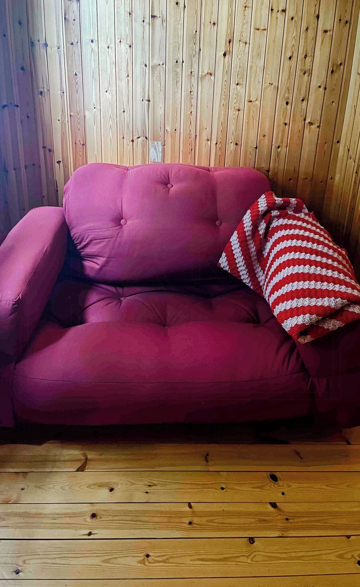 Un divano rosso con un cuscino a righe davanti a una parete in legno.