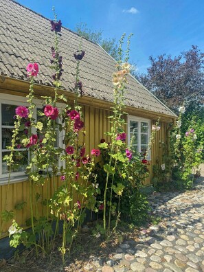 Ein hölzernes Haus mit Ziegeldach, umgeben von einem Garten mit blühenden Pflanzen.