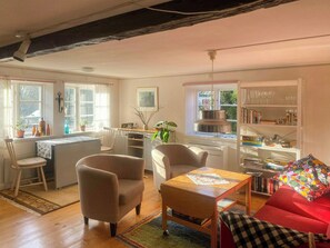 Ein gemütliches Wohnzimmer mit Holzboden, einem roten Sofa, einem Holztisch und einem Bücherregal voller Bücher und Dekorationsgegenstände.