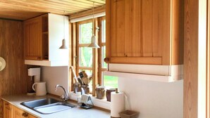 A kitchen with wooden cabinets, a double sink, a coffee maker, and a window with a view of greenery. - Lovely summerhouse by Sejerø Bay (Vig)