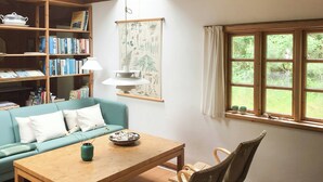 A cozy room with a wooden ceiling, a teal sofa, a wooden table, a bookshelf, and a window with a view of greenery. - Lovely summerhouse by Sejerø Bay (Vig)