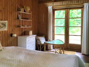 Ein Zimmer mit Holzboden, einem Bett, einem Schminktisch, einem Stuhl, einem Tisch und einem Fenster mit Vorhängen.