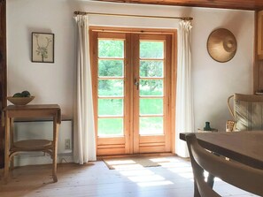 Una habitación con puerta de madera, una pequeña mesa con un cuenco, una silla y un adorno en la pared.