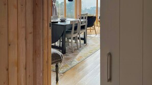 Un interior de madera con zona de comedor, ventanas amplias y vistas al exterior.