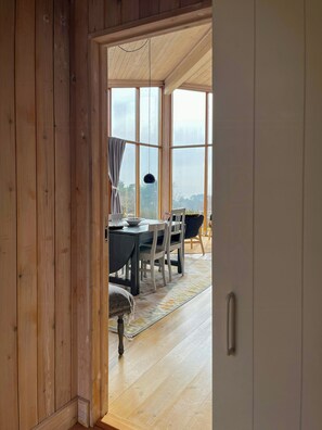 Ein Holzinterieur mit Essbereich, großen Fenstern und Blick ins Freie.
