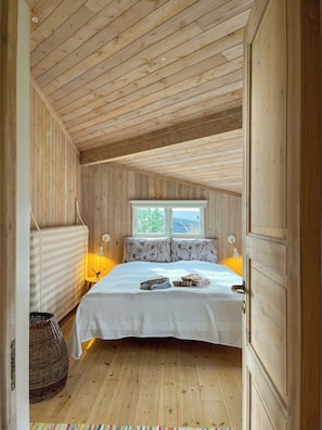 Ein Schlafzimmer mit Holzwänden, einem Bett, zwei Nachttischlampen, einem Fenster und einer Tür.