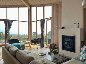 Ein geräumiges Wohnzimmer mit Kamin, großen Fenstern und Blick ins Freie.