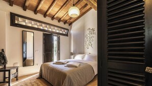 Ein Schlafzimmer mit einem Bett, einem Spiegel, einer Holzbalkendecke und einem Fenster.