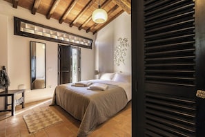 Ein Schlafzimmer mit einem Bett, einem Spiegel, einer Holzbalkendecke und einem Fenster.