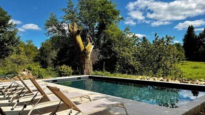 Piscina com espreguiçadeiras, cercada por árvores e céu claro.