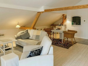 En hyggelig loftlejlighed med højt til loftet, synlige træbjælker, en hvid sofa, et lille bord og en fletstol.