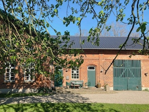 En murstensbygning med en grøn dør, et bord med stole og en stor, grøn port.