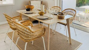 A dining area with wicker chairs, a table set for four, and a large window with a view of greenery. - Thatched holiday home by the Baltic Sea (Großenbrode)