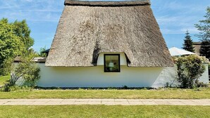 A thatched-roof cottage with a small window, surrounded by greenery and a clear sky. - Thatched holiday home by the Baltic Sea (Großenbrode)