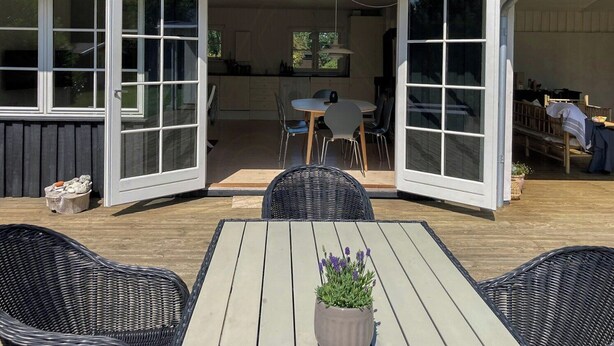 En åben patio med spiseplads, fletmøbler og en potteplante.