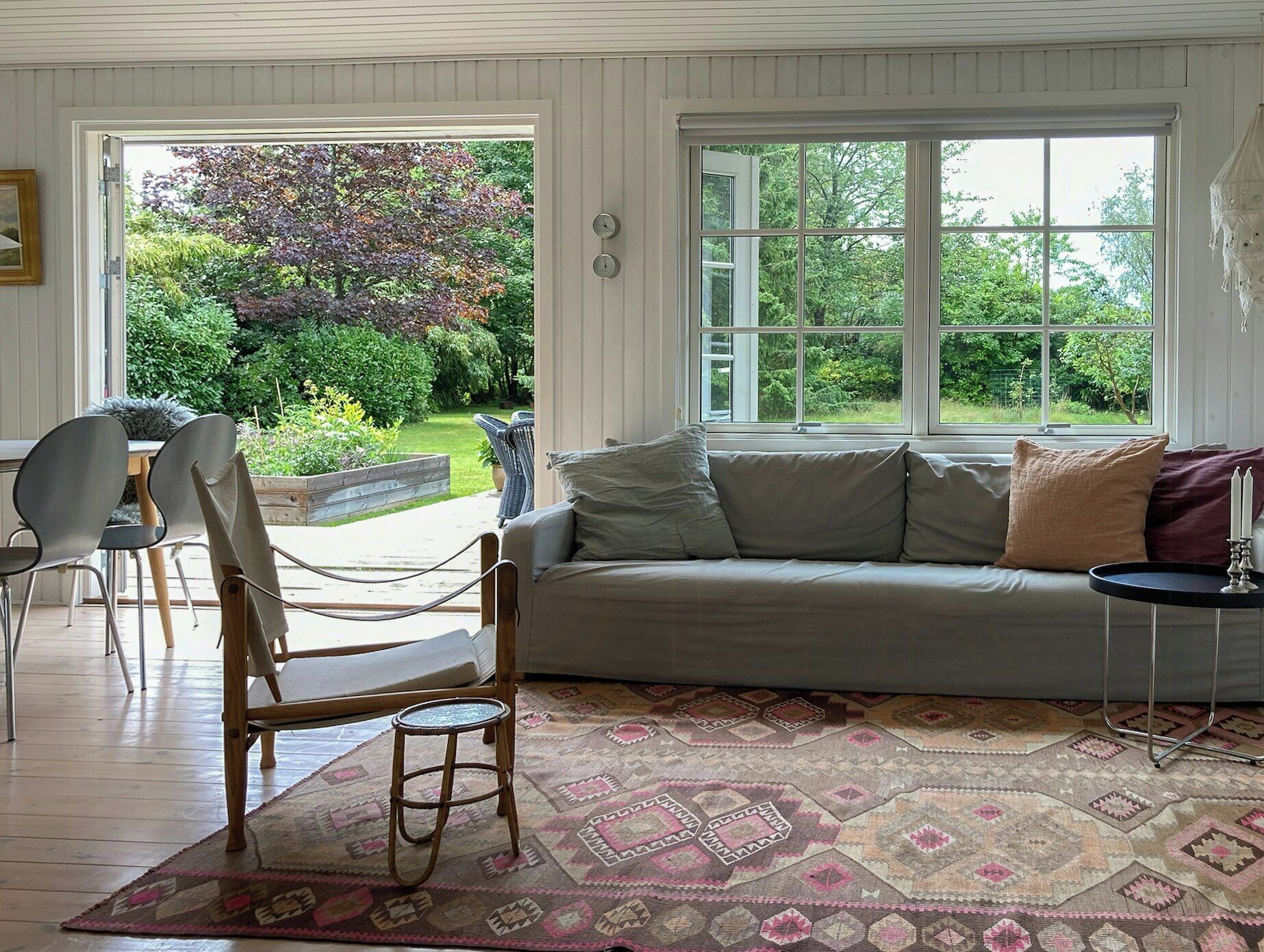 A room with a sofa, a chair, a small table, and a window with a view of greenery.