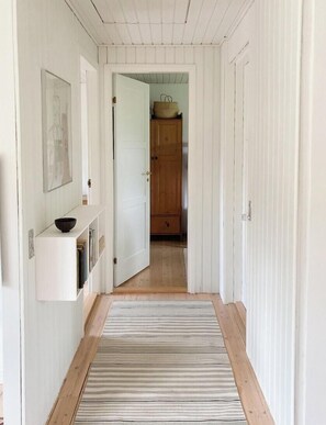 Ein Korridor mit Holzboden, weißen Wänden, einem Streifenmuster-Teppich, einem Holzkasten und einer Tür zu einem weiteren Raum.