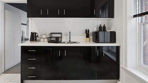 A modern kitchen with black cabinets, a white countertop, and a window with blinds. - Hobart CBD Loft - Walking to CBD (Hobart)