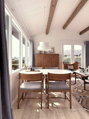 A dining area with wooden chairs and a table, a wooden cabinet, and a hanging light fixture. - Beach villa overlooking South Funen Archipelago (Faaborg)