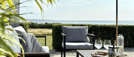 Un área de estar al aire libre con vista al mar, una mesa con bebidas y un paraguas grande.