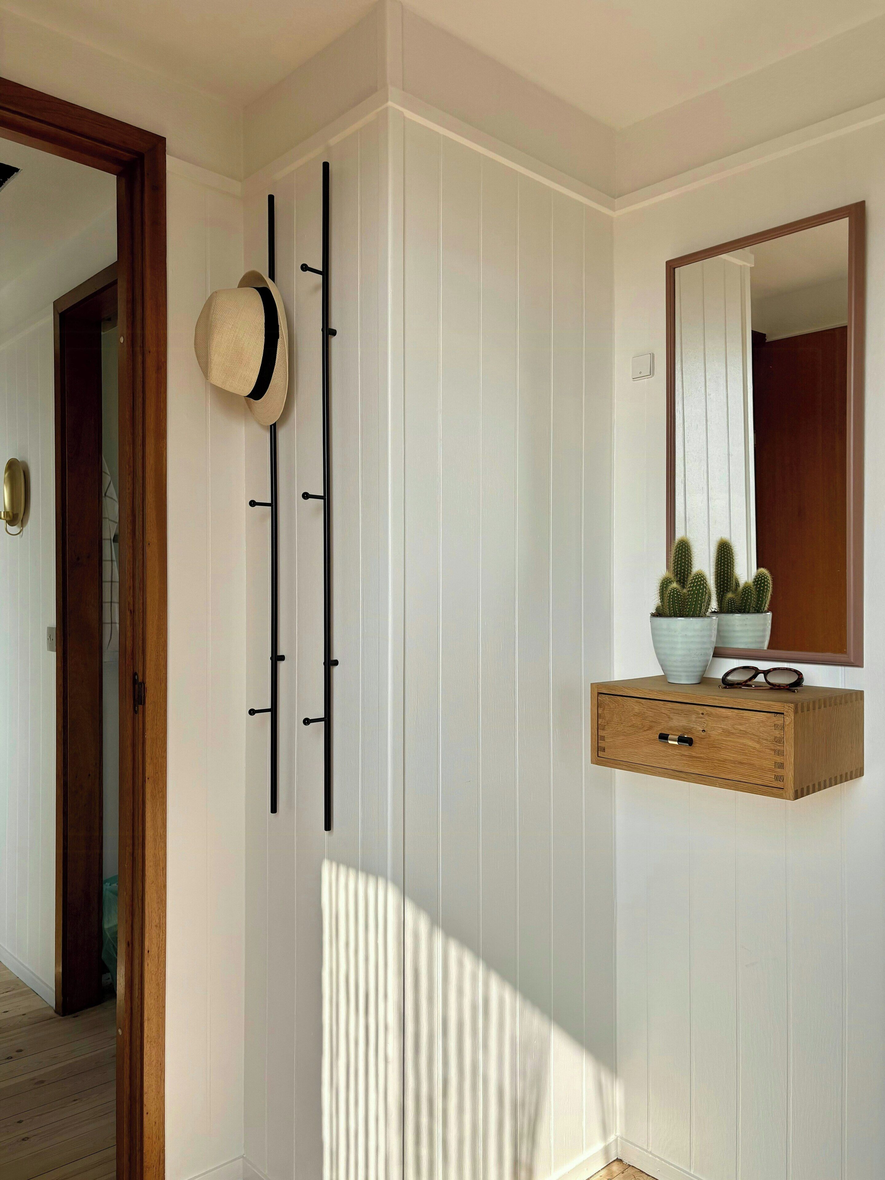 Un pasillo con una puerta de madera, un perchero en la pared, un espejo y un mueble de madera con una planta de cactus.