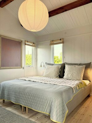 A bedroom with a bed, a hanging light fixture, two windows with bamboo blinds, and a chalkboard wall. - Beach villa overlooking South Funen Archipelago (Faaborg)