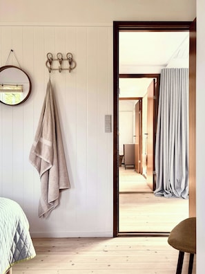 A room with a wooden floor, a bed with a quilted cover, a towel hanging on a hook, and a door leading to another room. - Beach villa overlooking South Funen Archipelago (Faaborg)