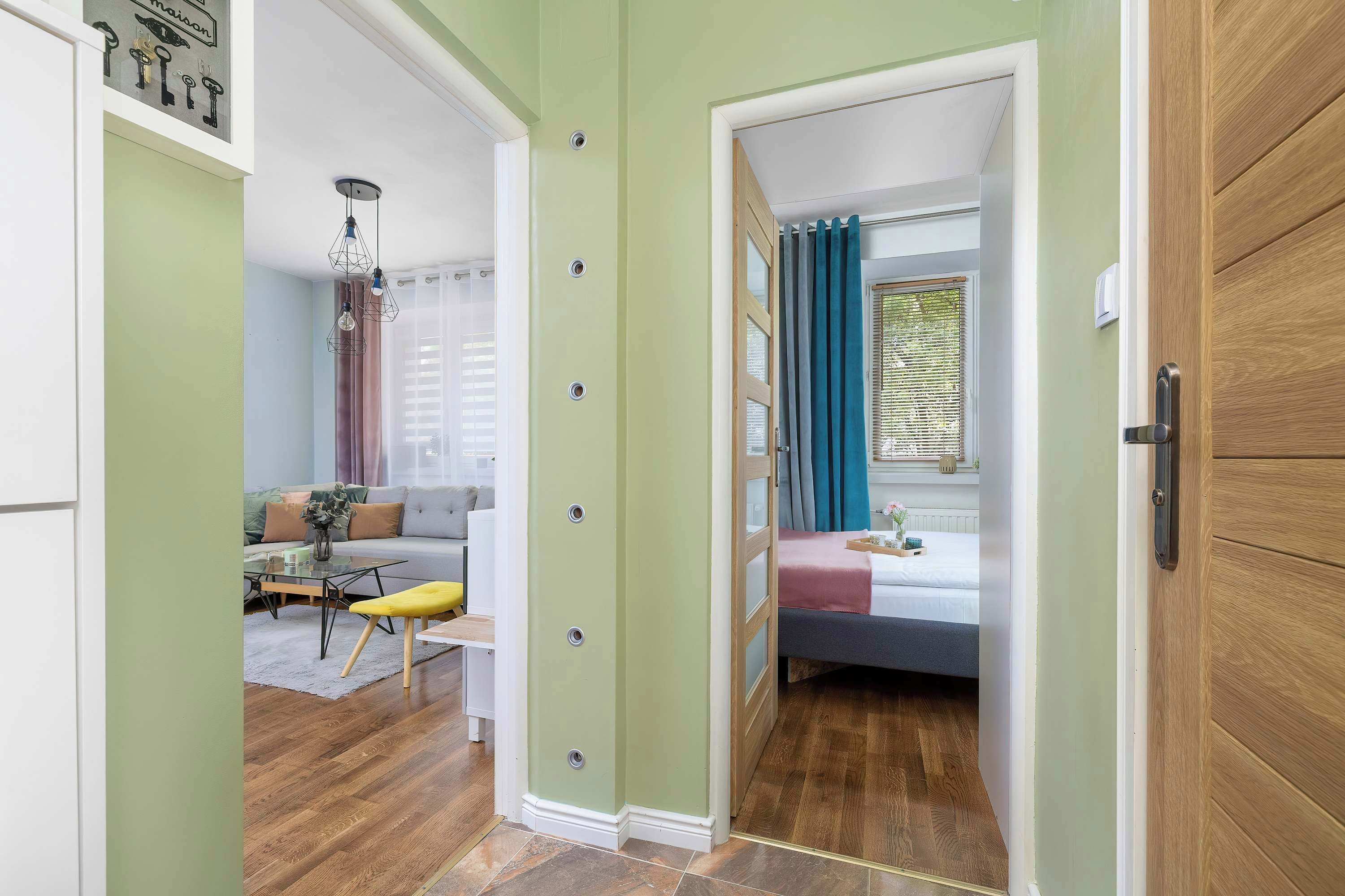 Une pièce comprenant un lit, une fenêtre avec des rideaux, une porte en bois et un couloir menant à une autre pièce.