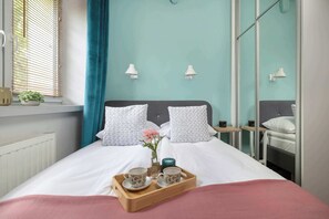 A neatly made bed with white bedding, a bedside table with a cup and saucer, a small vase with flowers, and a tray with two cups. - Cozy Apartment | Near the Banksy Museum (Kraków)