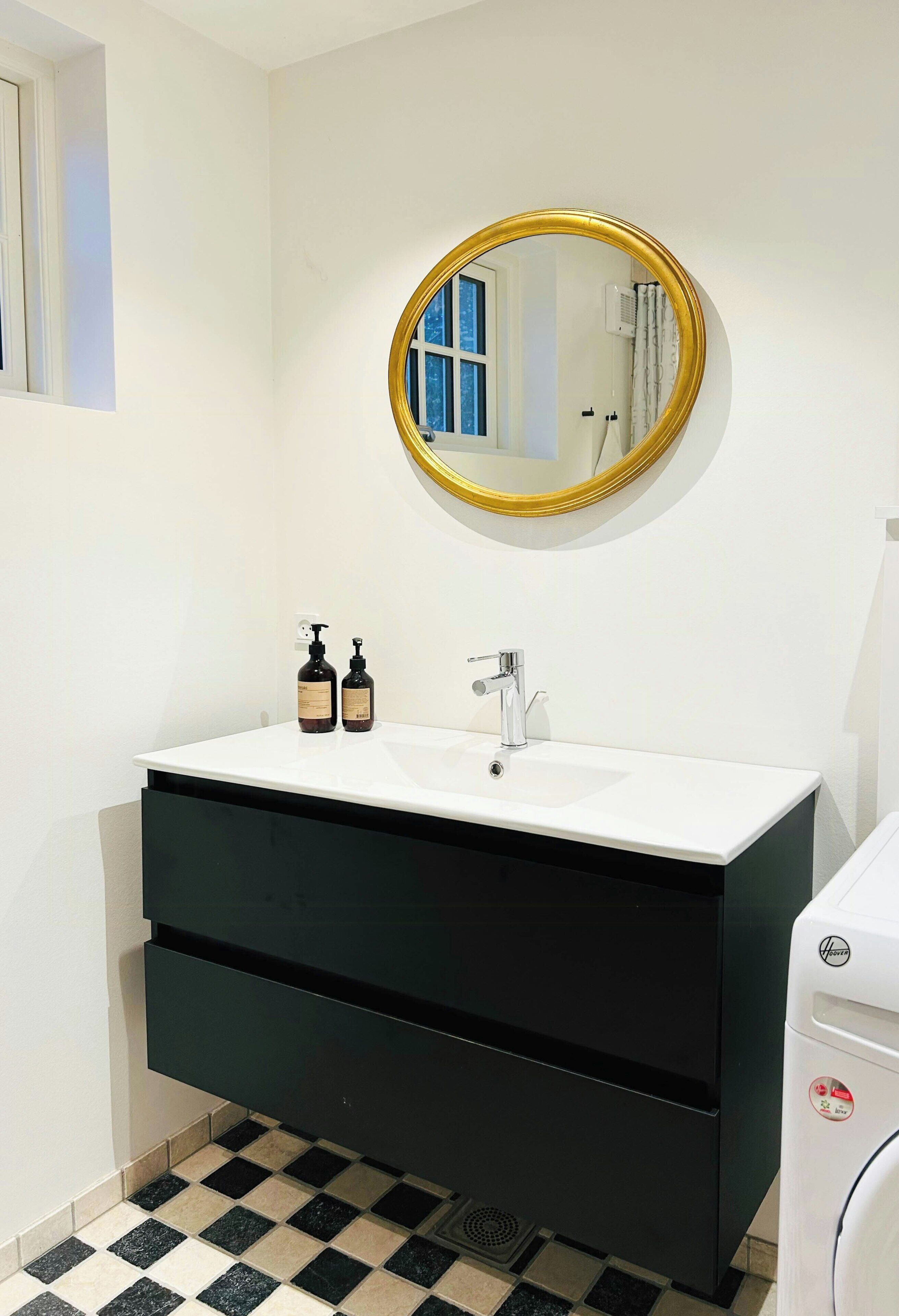 A bathroom with a white sink, black vanity, a gold-framed mirror, and a checkered floor.