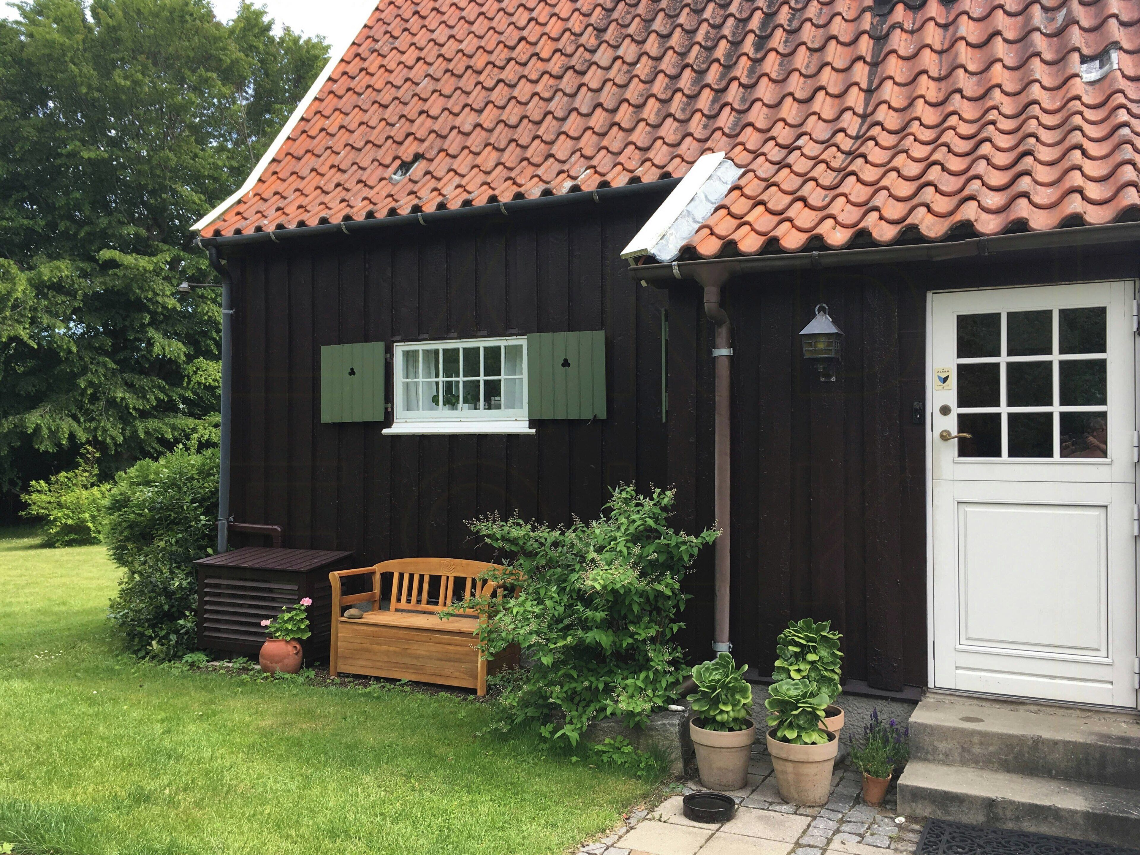 A wooden house with a tiled roof, a white door, and a small porch with a bench.