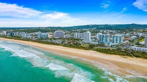 Eine Luftaufnahme einer Küstenstadt mit Sandstrand, Hochhäusern und blauem Himmel.