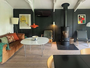 Ein gemütliches Wohnzimmer mit einer Couch, einem Tisch, einem Sessel, einem schwarzen Kaminofen und einem gerahmten Bild an der Wand.