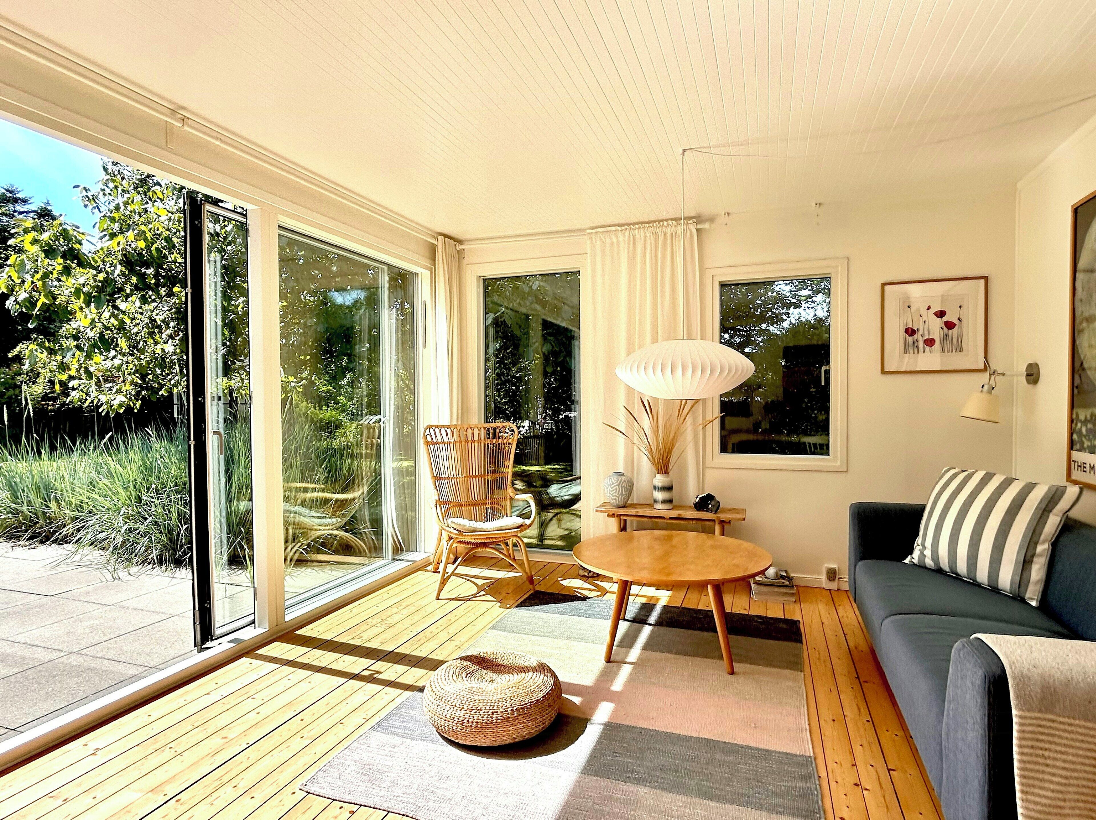 A modern living room with a sofa, a round table, a wicker chair, and a large window.