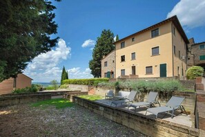 Ein zweistöckiges Gebäude mit einer Stein-Fassade, einer Terrasse mit Sitzgelegenheiten und Blick auf die Landschaft.