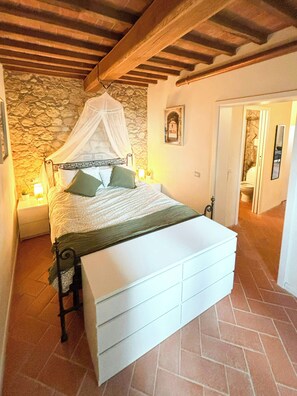 Ein Schlafzimmer mit Steingemäuer, einem Baldachinbett, einem weißen Nachttisch und einem Beistelltisch.