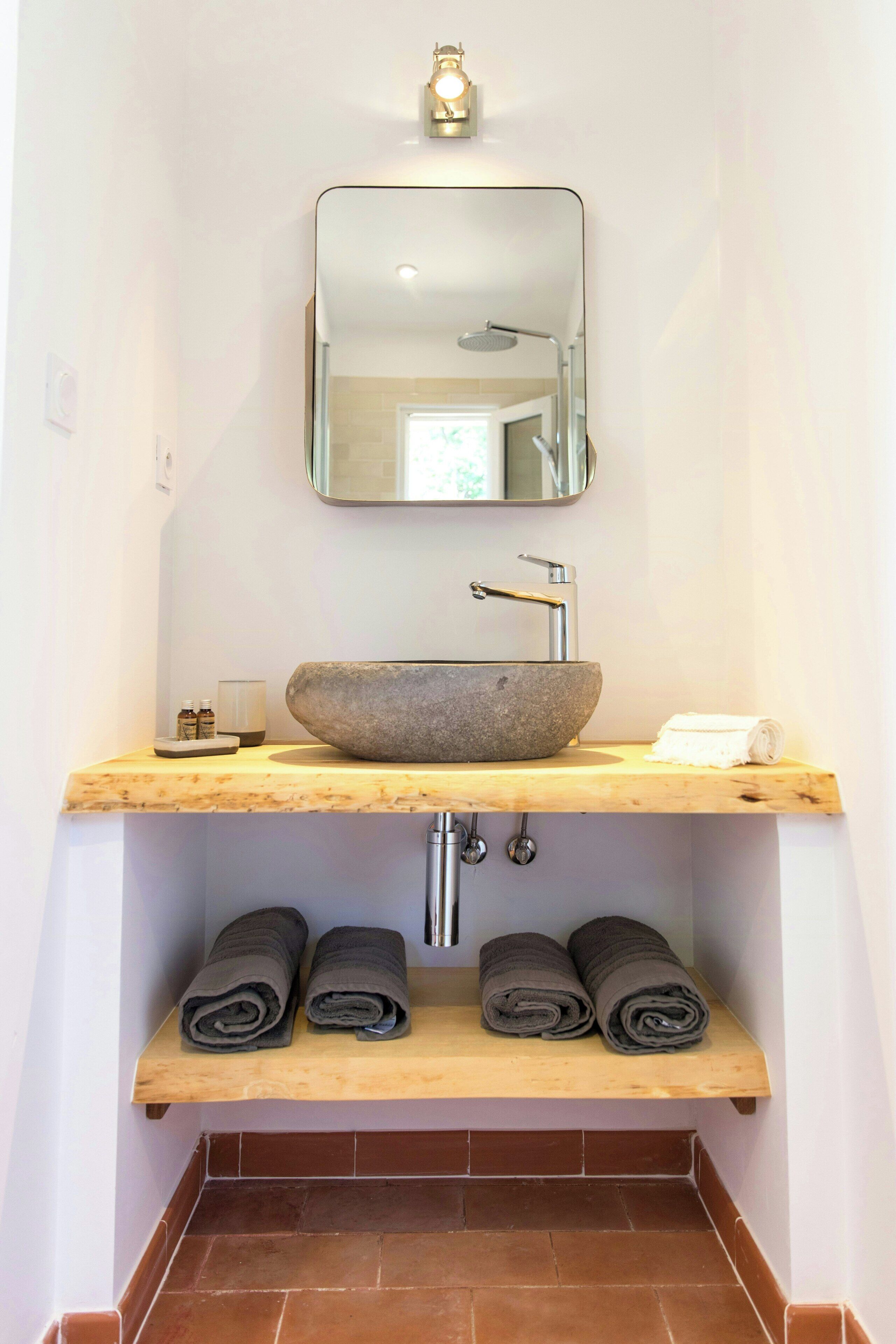 Une salle de bain avec un lavabo en pierre, un miroir, un porte-serviettes et une étagère avec des serviettes.