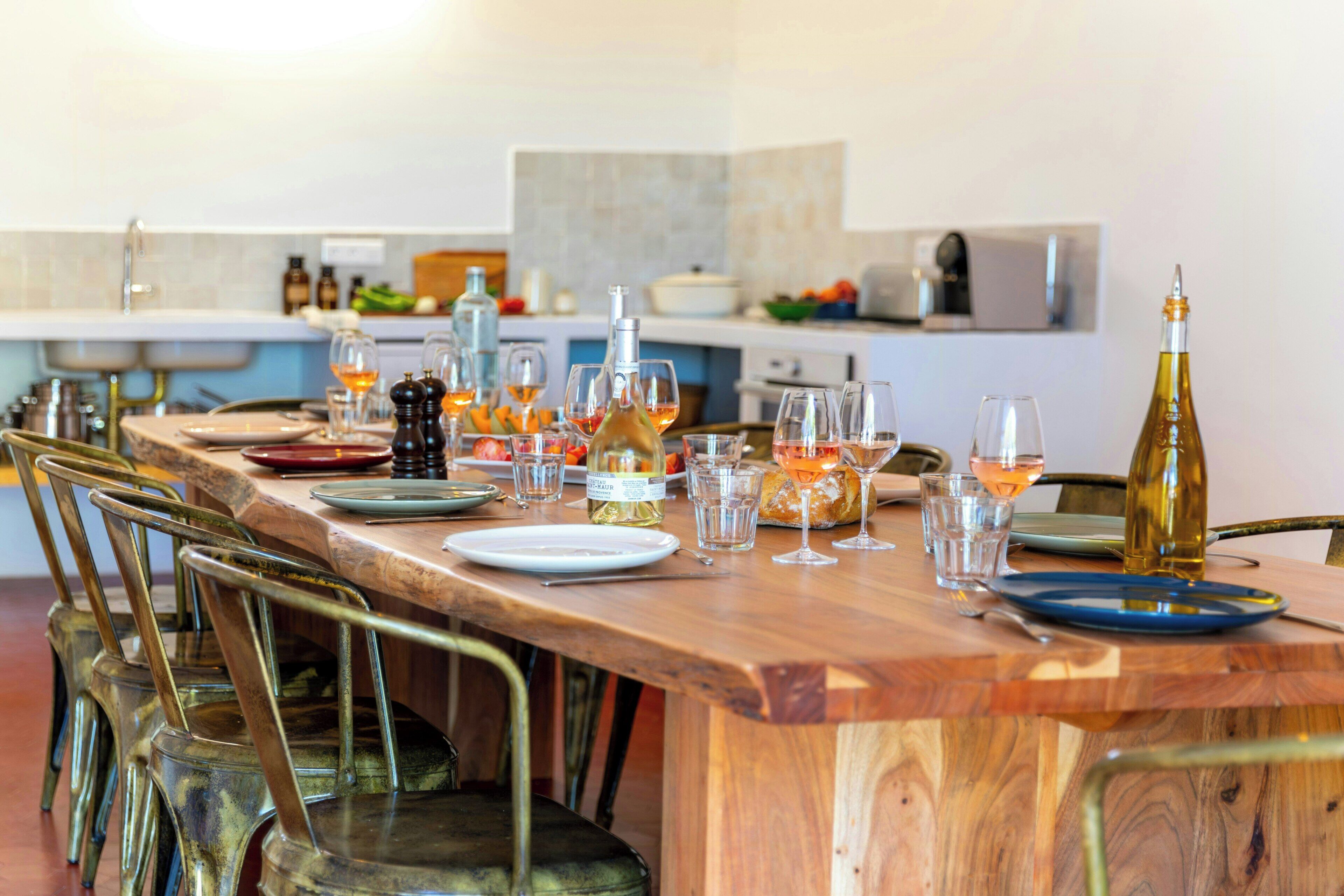 A wooden dining table set with plates, glasses, and bottles, surrounded by metal chairs.