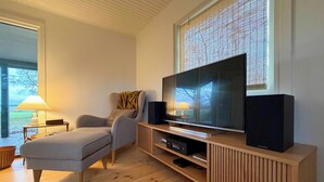 Una sala de estar moderna con televisor de pantalla plana, mueble de entretenimiento de madera, sofá gris y una ventana con persianas.