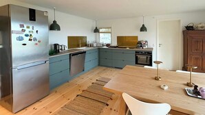 Una cocina moderna con un refrigerador de acero inoxidable, lavavajillas, un lavamanos y una mesa de comedor de madera con sillas.