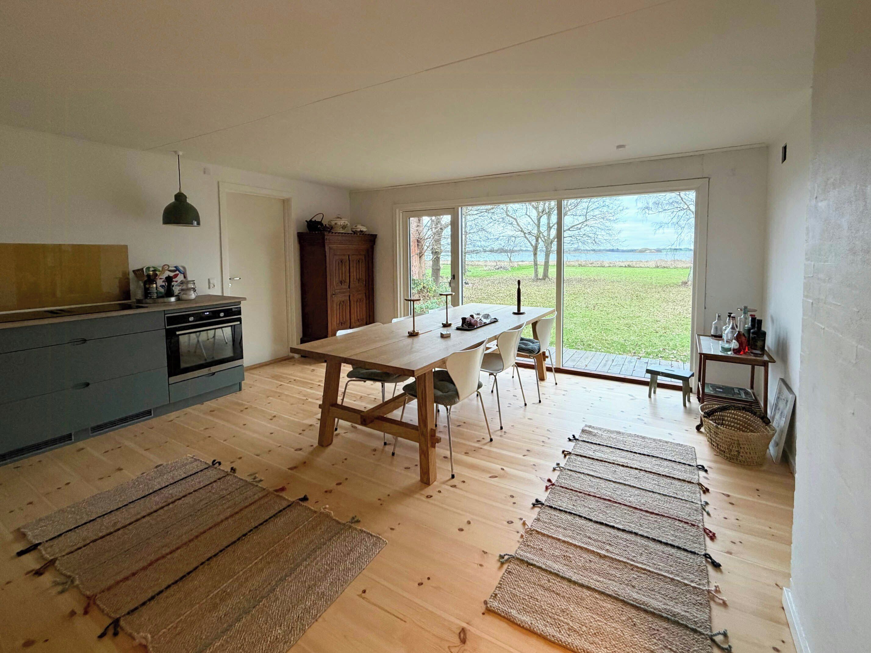A modern kitchen with a dining area, large windows, and a view of the outdoors.